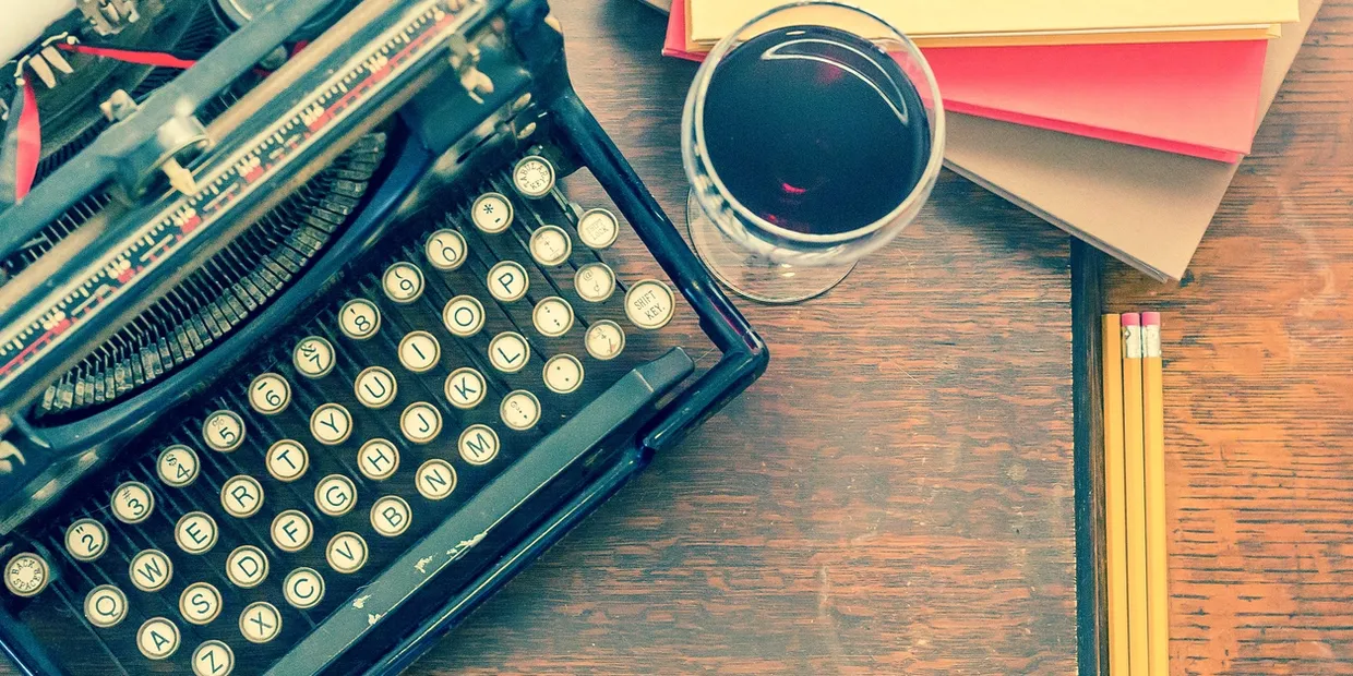 A table with an old fashioned typewriter and glass of wine.