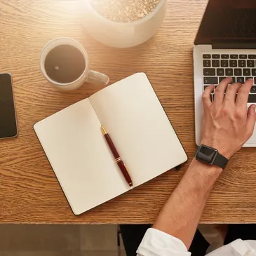 A person sitting at a desk with a laptop and coffee.