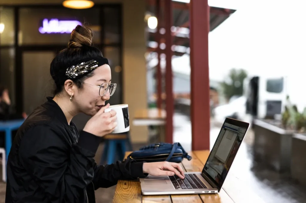 A woman sitting at a table with her laptop and coffee.